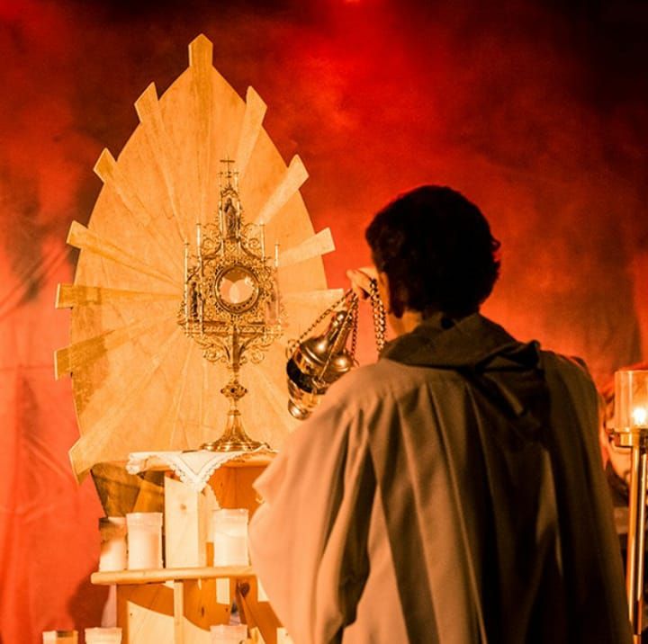 Ministrant beweihräuchert Monstranz auf Podest, warmer orangener Hintergrund