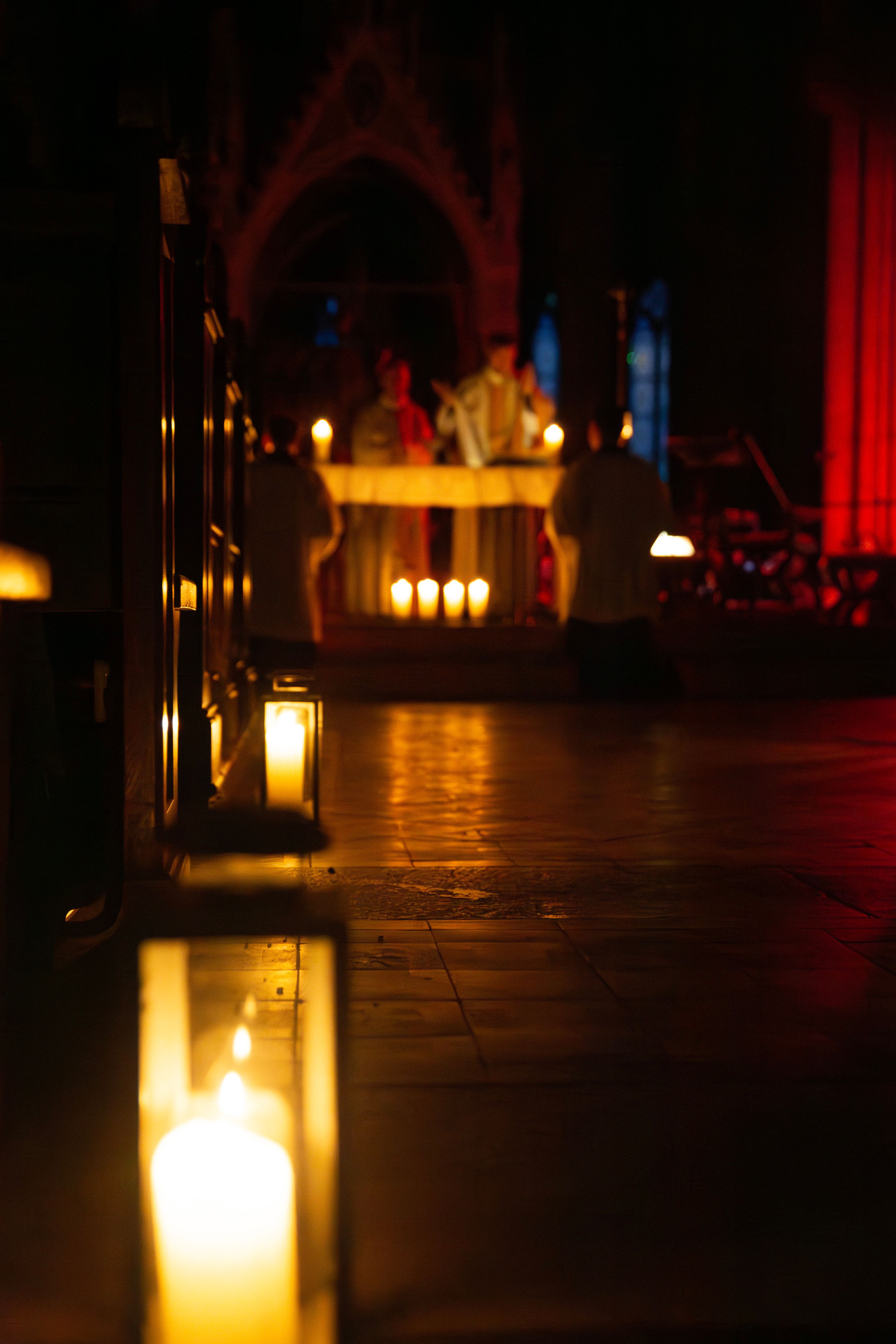 Brennende Lichter in dunkler Kirche sind im Mittelgang einer Kirche aufgestellt. Zwei Priester feiern die Heilige Messe im Advent als Rorate Messe