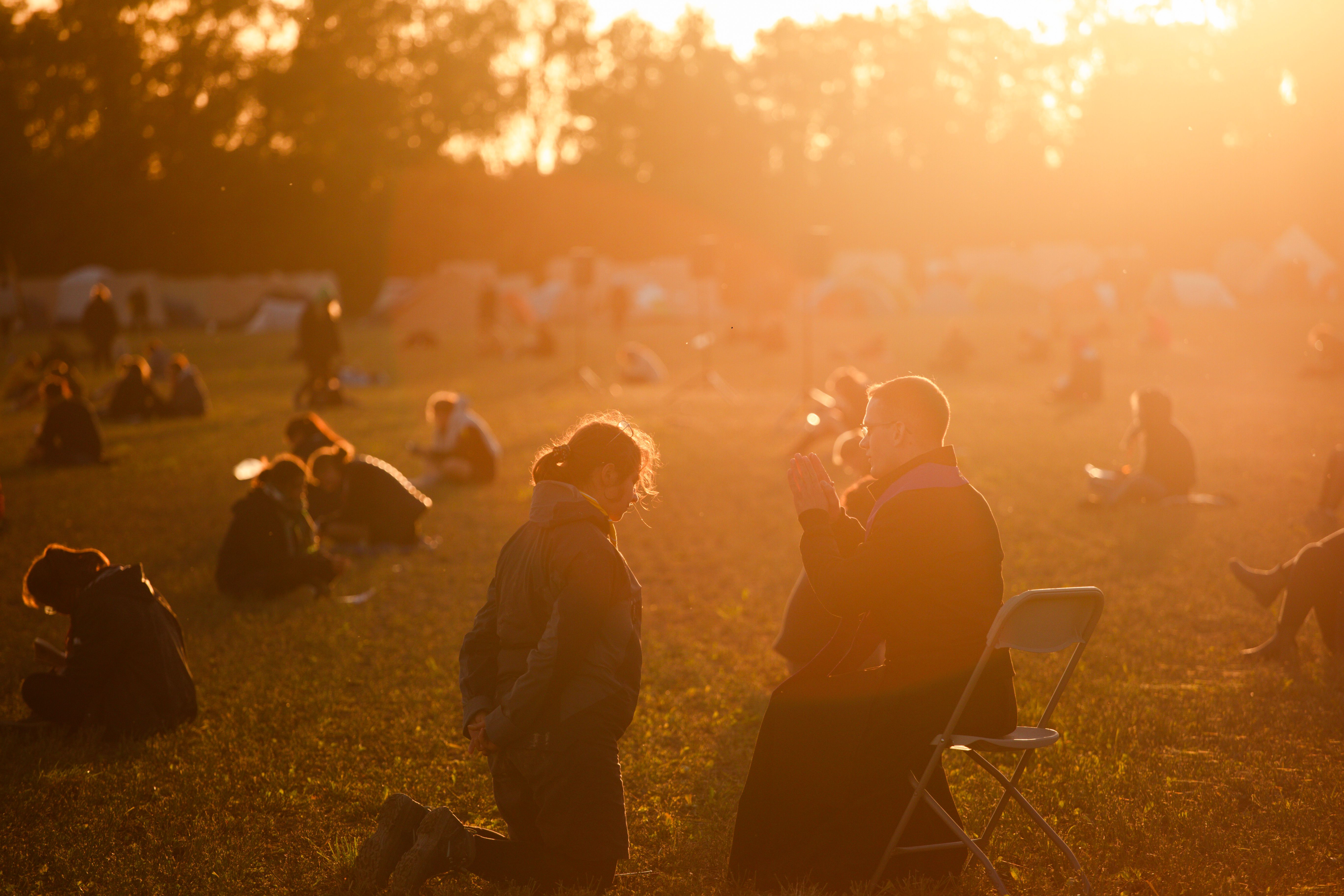 wunderschöne Abendsonne strahlt auf Feld; dieses ist voll an jungen Menschen, die das Sakrament der Beichte empfangen