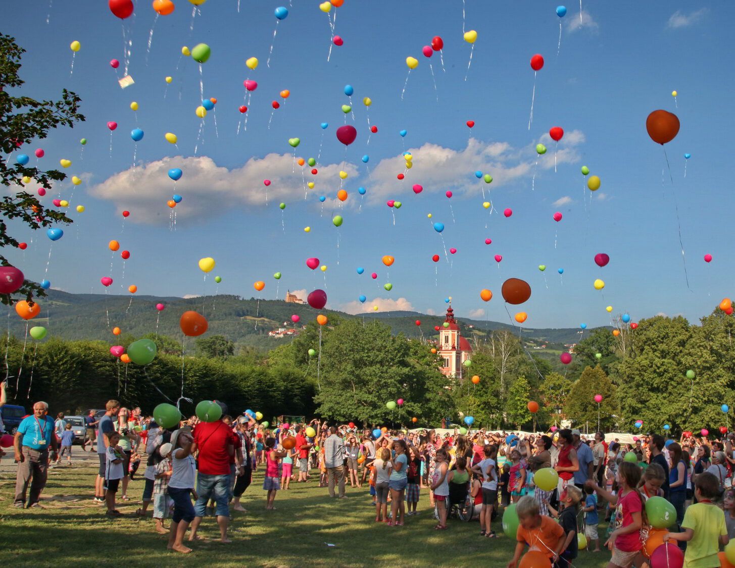 Families are standing in a meadow in Pöllau or Krems, colorful balloons rise into the sky
