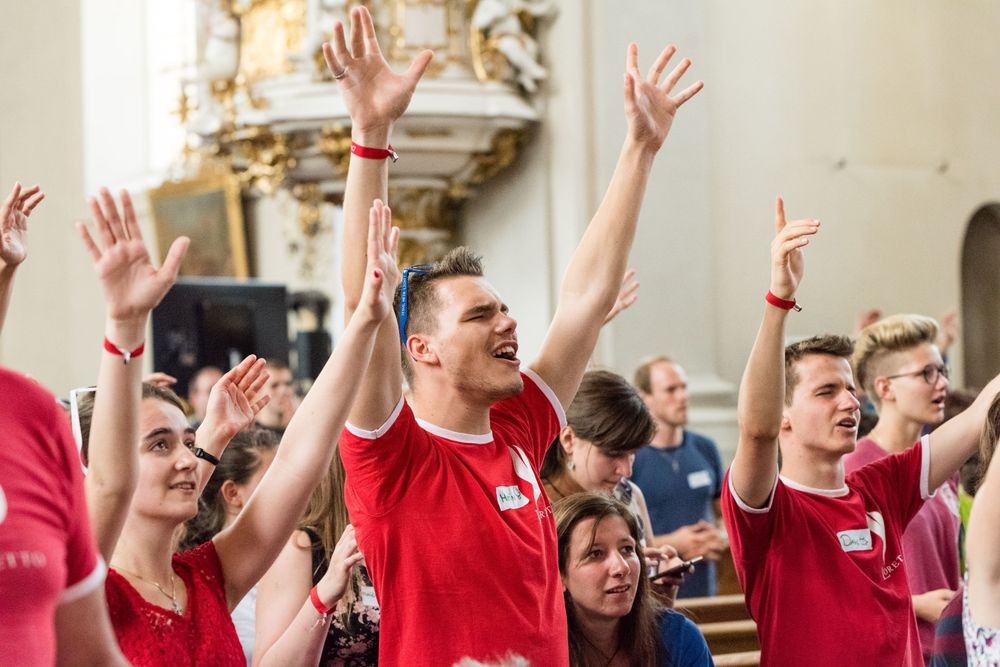 charismatischer Lobpreis, junge Katholiken in roten Shirts singen freudig und strecken die Hände in die Luft