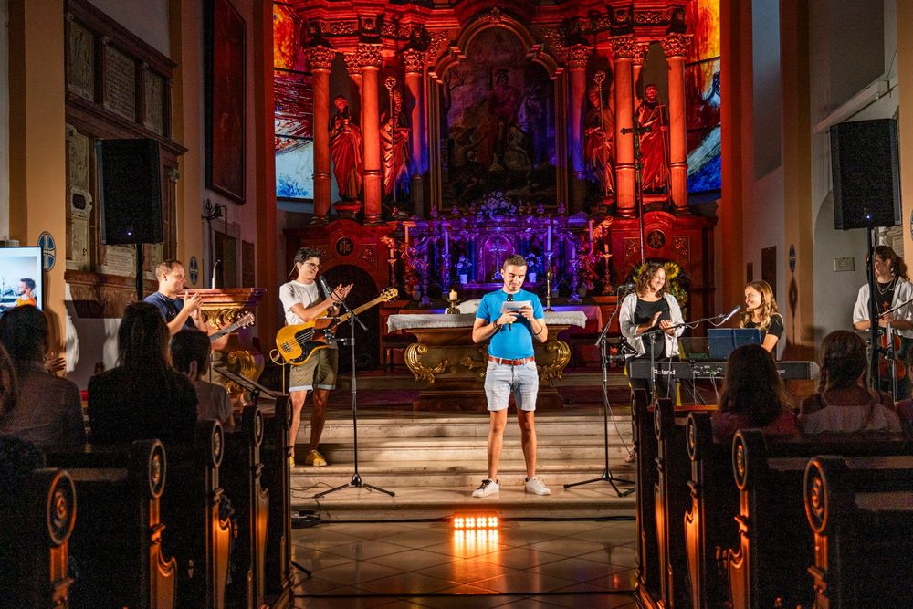 moderne katholische Kirchenmusik, Band spielt in Kirche, Altar ist beleuchtet, Bänke sind voll von Jugendlichen