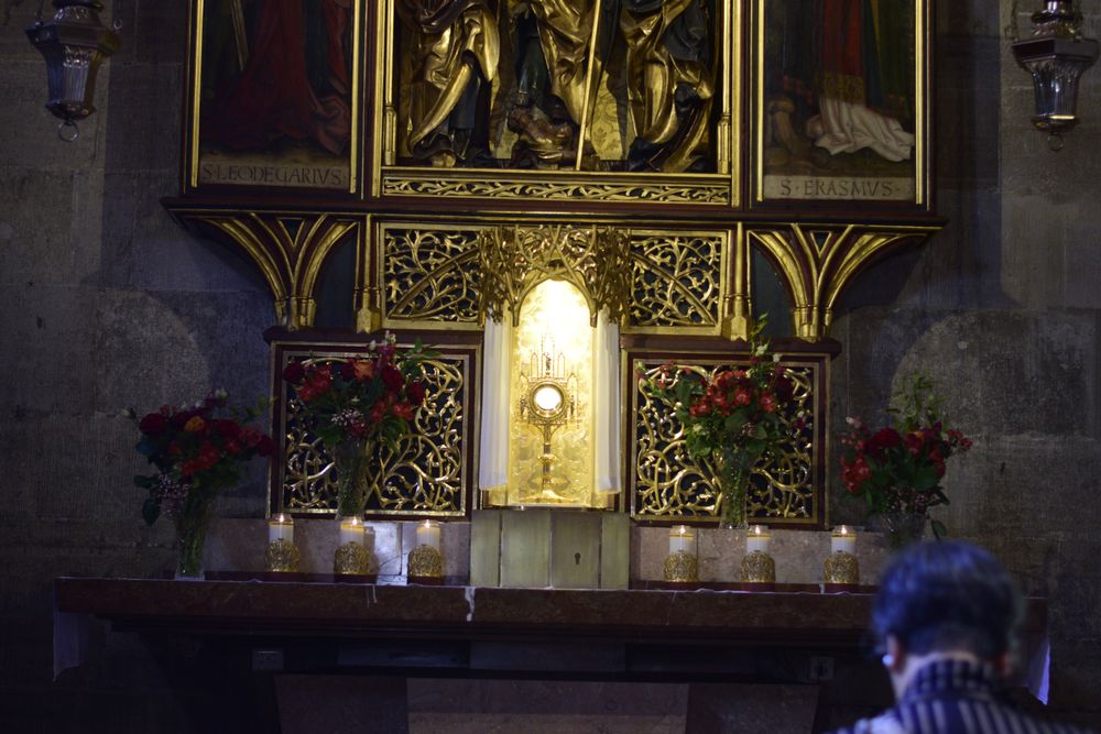 gotischer Altar in Seitenkapelle des Stephansdoms, Monstranz mit Allerheiligstem strahlt; Frau kniet in Bank und betet an