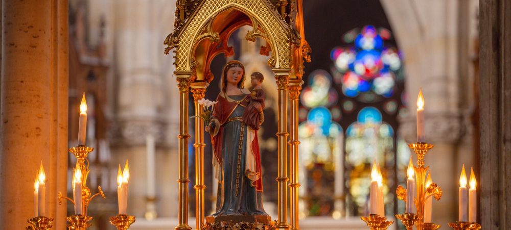 Marienstatue umrahmt von warmen Kerzenlicht in gotischer Kathedrale