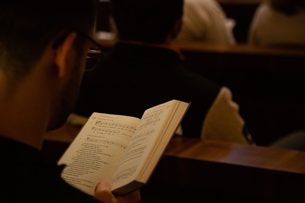 Laudes, Komplet, junger Mensch singt und betet in Kirchenbank