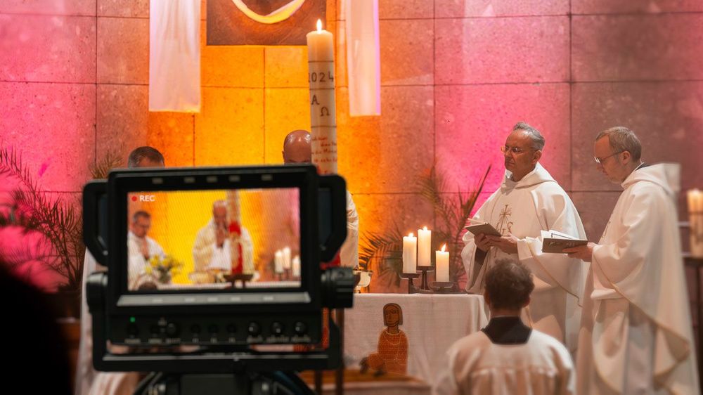 im Vordergrund ist eine Kamera, die mehrere Priester bei der heiligen Messe filmt und per livestream sendet