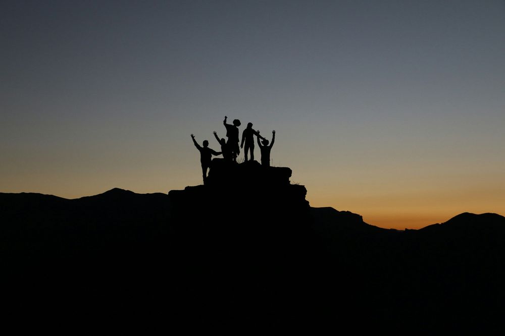 Menschen die jubelnd auf einem Berg stehen bei Sonnenuntergang